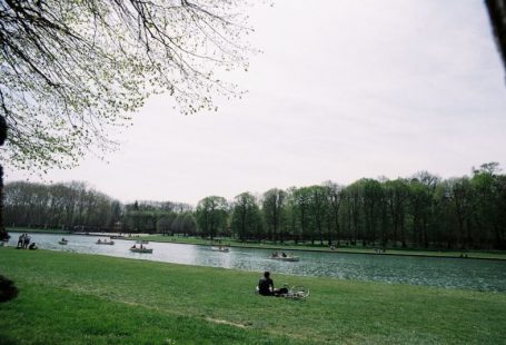 Europe Landscape - a person sitting on a blanket by a lake with boats on it