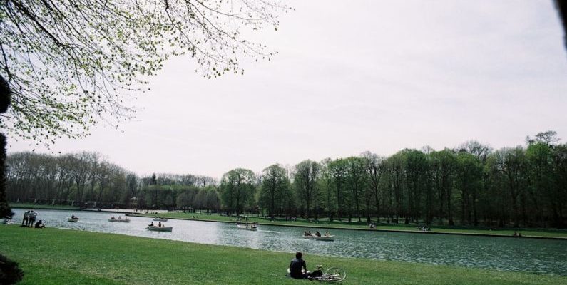 Europe Landscape - a person sitting on a blanket by a lake with boats on it