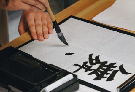 Chinese Calligraphy - person holding black paint brush while painting black text on white paper