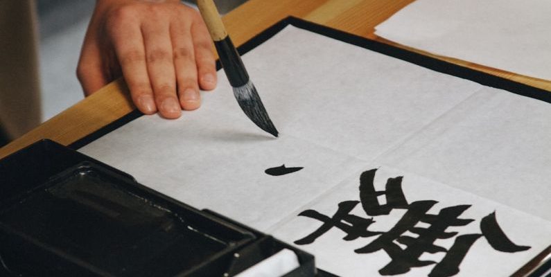 Chinese Calligraphy - person holding black paint brush while painting black text on white paper