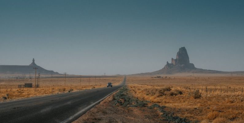 American Road Trip - a car driving down a road in the middle of the desert