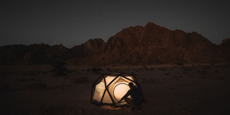 Solo Destination - a person sitting inside of a tent in the desert